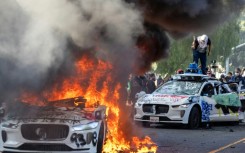 Demonstrators smash the windshield of a vehicle next to a burning self-drive vehicle as protesters clash with law enforcement in Los Angeles, California, on June 8, 2025