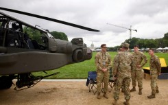Soldiers gather next to an US Army AH-64 Apache helicopter on display on the National Mall during the Army 250th anniversary celebration