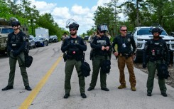 Police officers stand guard as demonstrators protest US President President Donald Trump's visit to "Alligator Alcatraz"