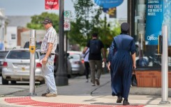 A woman dressed in traditional Mennonite clothing walks through the downtown of Aylmer, Canada in July