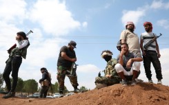 Tribal fighters stand next to a government checkpoint east of Sweida city, in southern Syria