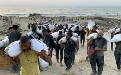Palestinians carry bags of flour from aid convoys in the Israeli-controlled Zikim border crossing in the northern Gaza Strip