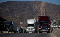 Cargo trucks queue next to the border wall before crossing into Tijuana, Mexico