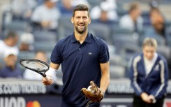Tennis star Novak Djokovic carries his racquet to the mound before throwing the ceremonial first pitch at a New York Yankees baseball game