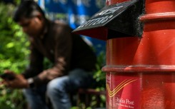 A man uses his mobile phone while sitting next to an India Post box outside its office in New Delhi