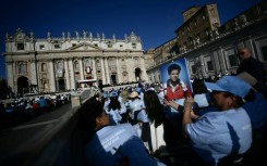 A faithful holds a portrait of late teenager Carlo Acutis in front of Saint Peter's