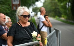 A woman holds a white rose as she waits for the hearse carrying the body of Giorgio Armani