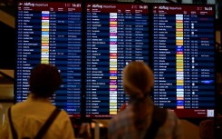 Passengers check a digital display showing flights at Berlin Brandenburg BER airport