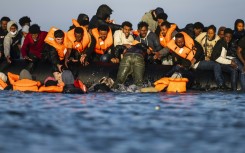 Migrants sitting in a smugglers' boat help others to climb on board in an attempt to cross the English Channel from northern France at the weekend