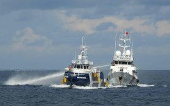 This handout photo taken and released on October 12, 2025 by the Philippine Coast Guard shows a China Coast Guard ship (R) deploying water cannon as a Philippine Bureau of Fisheries vessel (L) is seen alongside during an incident near Thitu island in disputed waters of the South China Sea
