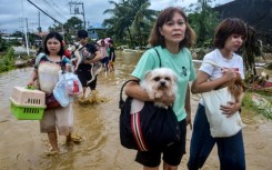 Residents carrying their belongings and pet dogs wade through a flooded street as they evacuate from their inundated homes in Liloan town, Cebu province