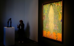 The piece represents the daughter of Klimt's main patron dressed in a white imperial Chinese dress, standing before a blue tapestry with Asian-inspired motifs