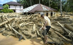A villager walks among a pile of logs in flood-hit Tukka village in Indonesia