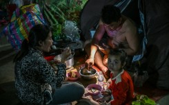 A displaced family uses a flashlight as they eat a meal at a temporary camp in Banteay Meanchey province on December 12, 2025, amid clashes along the Cambodia-Thailand border