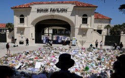 Mourners stand near tributes piled together at the front of the Bondi Pavilion, in memory of the victims of the Bondi Beach shooting