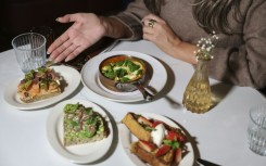 A patron poses at a table with an array of half-sized portions of meals that some restaurants are offering as more and more people have smaller appetites due to weight-loss drugs like Ozempic