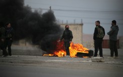 Kurdish fighters stand near burning tires at the entrance to the city of Tabqa in the northern Syrian Raqa province, on January 17, 2026