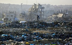 A Palestinian boy searches for recyclable material at a landfill against the backdrop of destroyed buildings in Khan Yunis, in the southern Gaza Strip