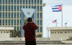 A tourist takes pictures of the US Embassy with the US flag and the Cuban flag in the background in Havana