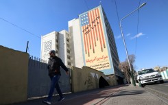 A man walks past a large anti-US mural on the side of a Tehran building