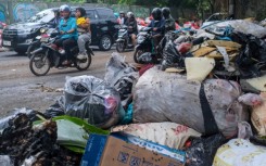 Vehicles driving along a road littered with illegally dumped waste in Pamulang, South Tangerang, Banten