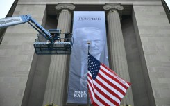 Workers on an aerial lift watch after installing a new banner featuring an image of US President Donald Trump on the facade of the US Department of Justice headquarters building in Washington, DC