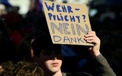 A student holds a sign reading 'Military conscription? No thanks'