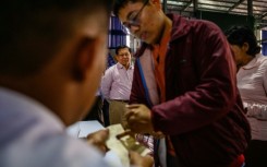 Military chief Min Aung Hlaing (back C) watches a voter ink their finger as he visits a polling station during the final phase of Myanmar's general election in January