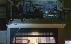A woman stands at a window as first responders and security forces inspect a damaged apartment above after the building was hit by an Iranian missile strike in Ramat Gan, on the outskirts of Tel Aviv, early on March 18, 2026