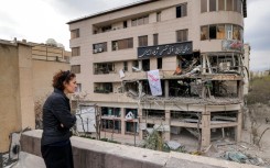 A woman standing on a rooftop in Tehran views destruction in an office building that housed the offices of the Doha-headquartered news network Al Araby TV following a missile strike on March 29, 2026