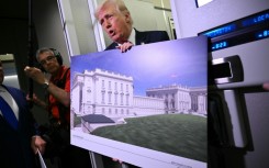 US President Donald Trump holds a rendering of the East Wing modernization as he speaks to reporters aboard Air Force One