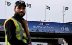 A policeman stands guard in front of a digital screen displaying news of US–Iran peace talks along a road in Pakistan's capital Islamabad