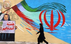 An Iranian woman walks past an anti-US and anti-Israel mural in Tehran