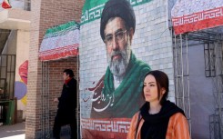 A woman walks past a large tiled image of Iran's current leader Ayatollah Mojtaba Khamenei outside a metro station in Tehran