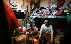 Guan Ci sits on his bed in his subdivided housing unit in Kowloon, Hong Kong