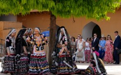 Artists wearing traditional attire and members of US Secretary of State Marco Rubio's team wait in the shade as he tours the Amber Fort in Jaipur