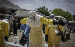 Health workers are doused with disinfectant after contact with the body of one presumed Ebola fatality