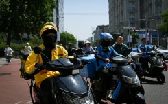 Food delivery workers on their vehicles on a street in Beijing