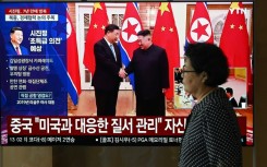 A woman walks past a television screen in Seoul Monday showing a news broadcast with file footage of the 2019 meeting between China's President Xi Jinping and North Korean leader Kim Jong Un
