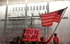 Protesters wave a US flag and hold a sign reading 'You're no JFK' as workers build scaffolding at the Kennedy Center ahead of the removal of Donald Trump's name
