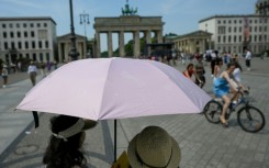 People shelter from the sun under umbrellas at Berlin's Brandenburg Gate
