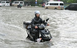 A man on a scooter makes his way along a flooded street in Beijing