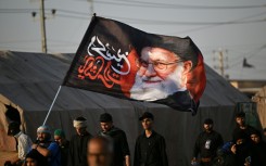 Shiite Muslim pilgrims hold a flag bearing the portrait of Iran's slain supreme leader Ayatollah Ali Khamenei as they march to the Iraqi city of Karbala