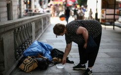 A woman puts some coins in a dish next to a man wrapped up with his dog on a London street