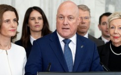 New Zealand Prime Minister Chris Luxon, flanked my his caucus, speaks to the media after surviving a second National party leadership vote at Parliament in Wellington on August 12, 2026