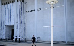 A person walks past scaffolding and a large protective tarp covering the facade of the John F. Kennedy Center for the Performing Arts